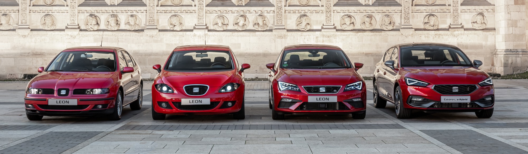quatre véhicules Seat Leon rouges alignés et garés sur une place extérieure